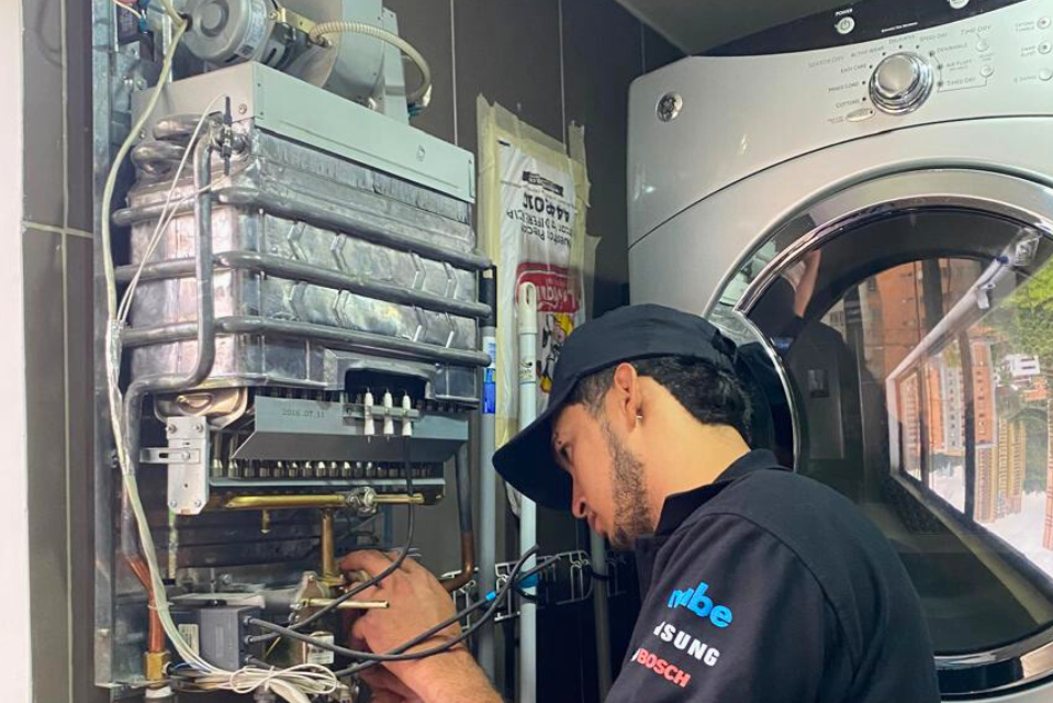 Técnico reparando calentador de agua en mantenimiento preventivo.